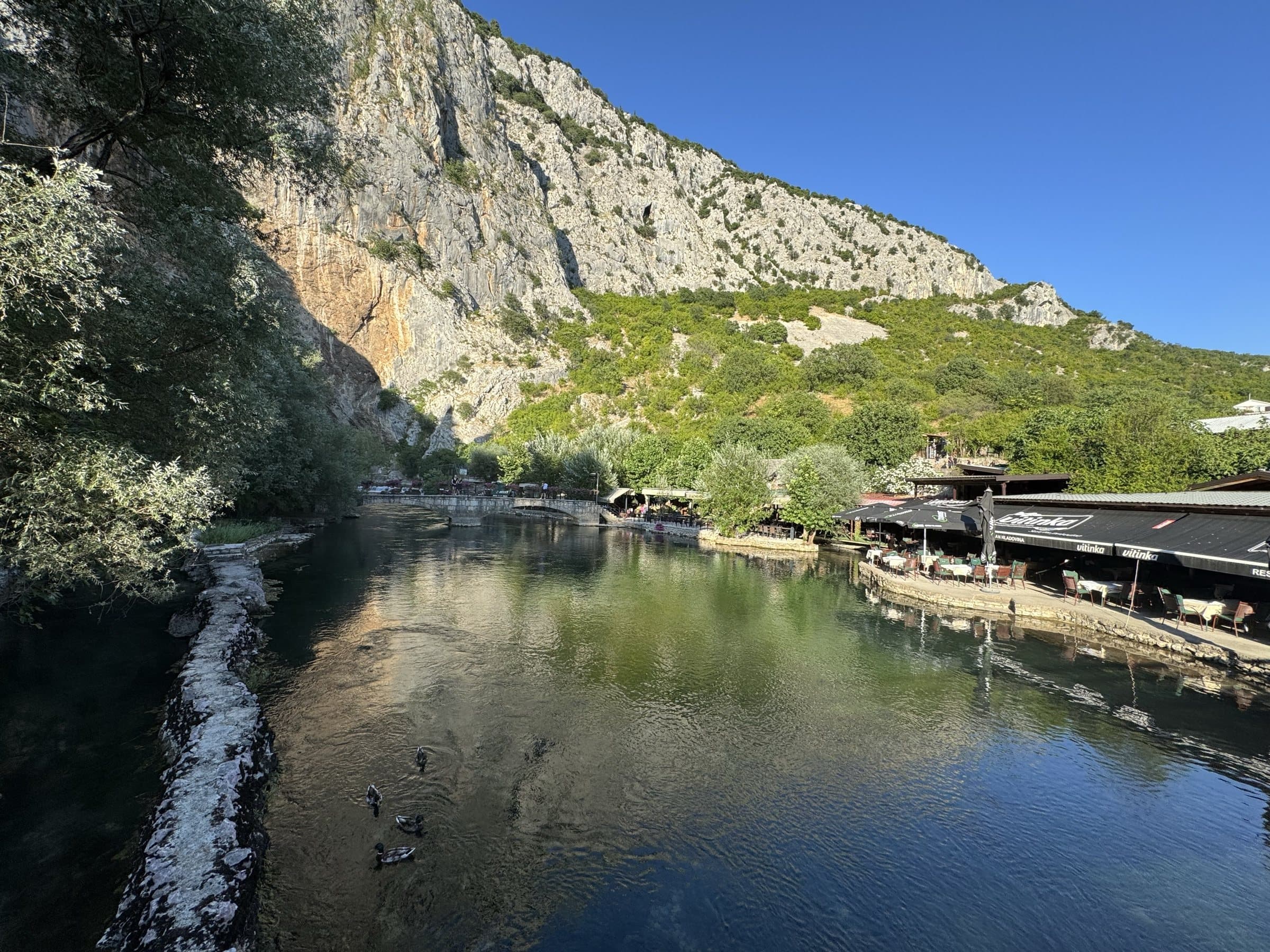 Riverside restaurant terraces along the clear green Buna at Blagaj, ducks on the water below the limestone cliff