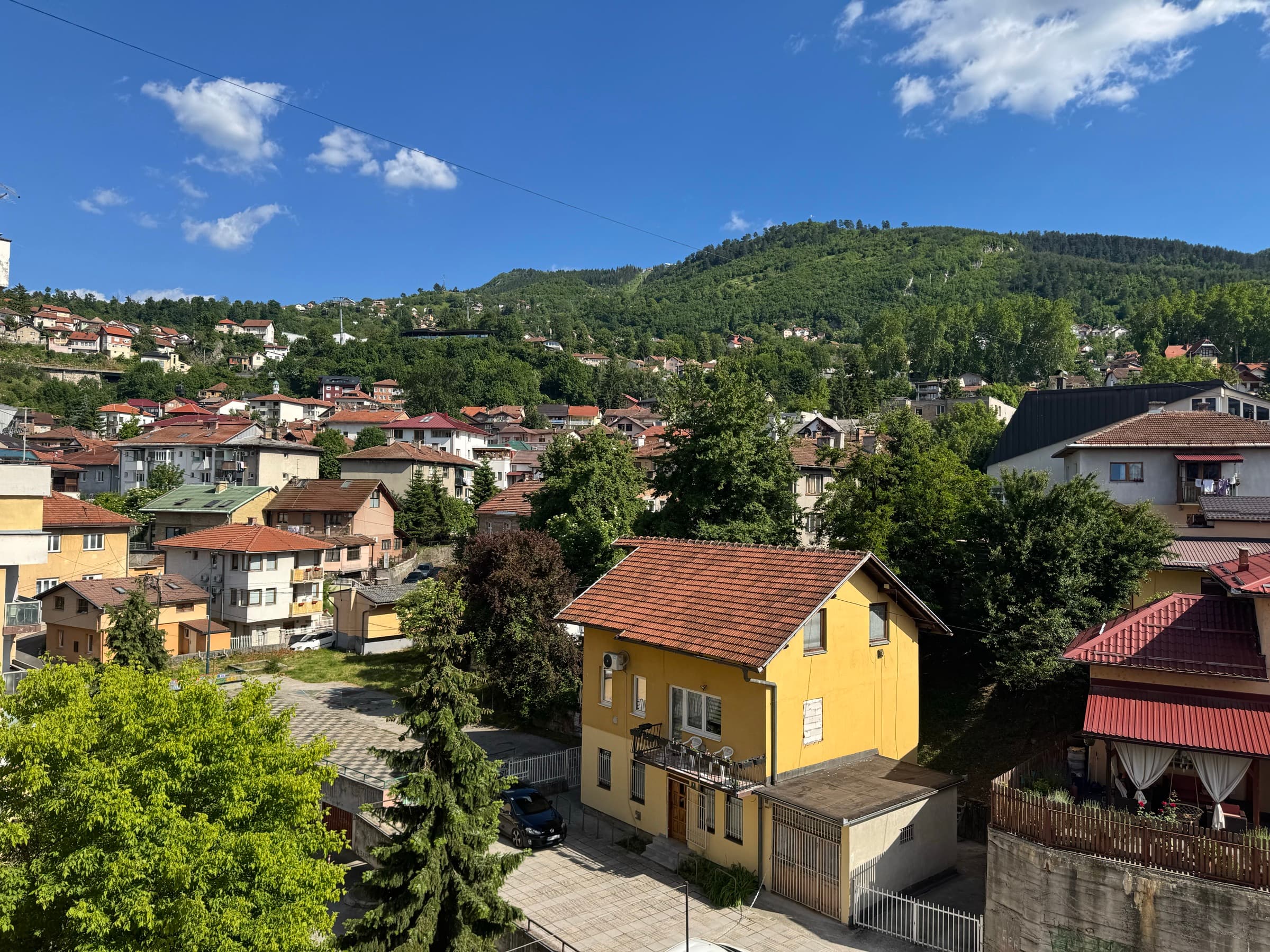 Morning over Sarajevo's old quarters — red-roofed houses climbing a green hillside with the mountain standing behind